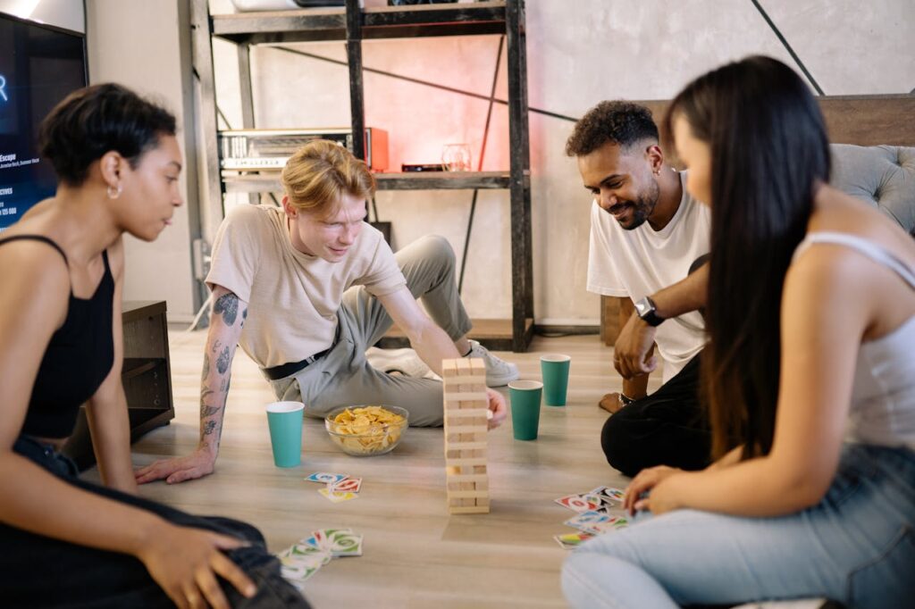 Four friends playing Friendsgiving games: Jenga and Uno on the ground