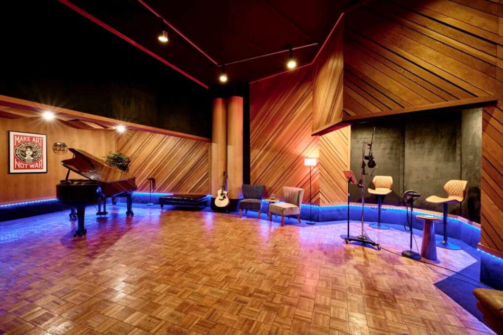 Large recording studio with a piano, guitar, two chairs and microphones, wooden walls and floors, and dim lighting