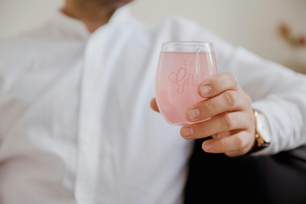 A pink drink in a small wine glass that says "It's a girl!"