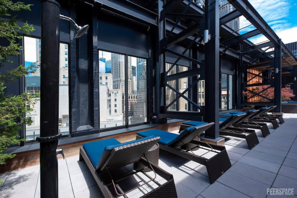 Lounge chairs sit by huge windows on a sun deck with views of New York City