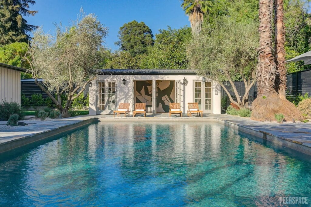 A pool house sits at the end of a long, rectangular pool glistening in the sunlight