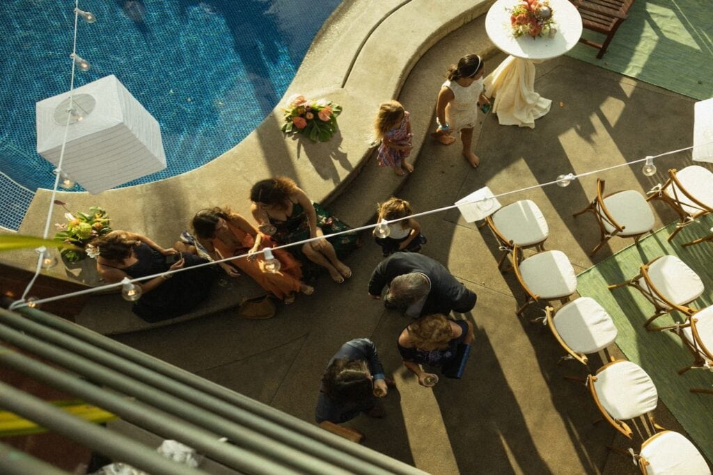 Overheard shot of a poolside reception with string lights, people milling about and flower arrangements