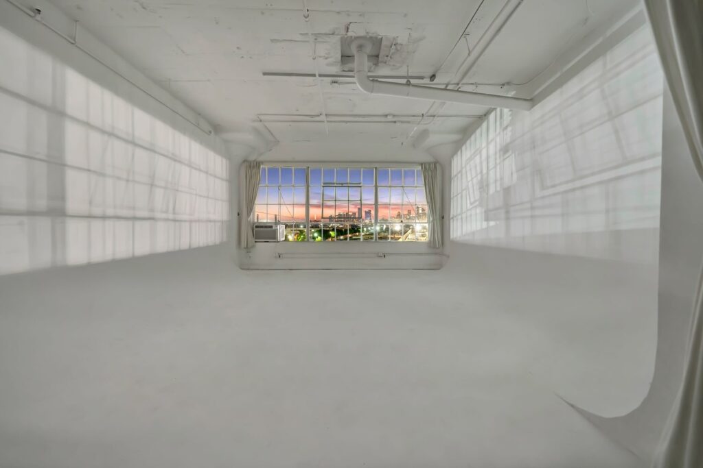 An all-white, industrial production space with a huge window overlooking the city at sunset