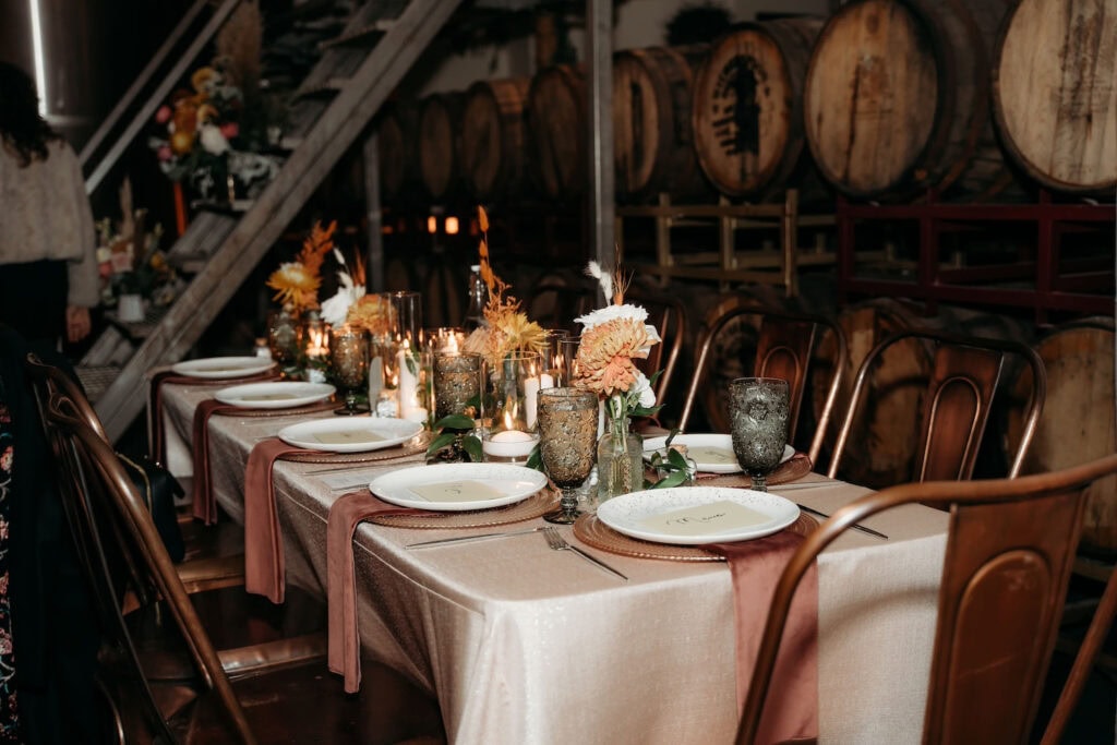 A simple reception table is set up with metal chairs by a wall of wine barrels