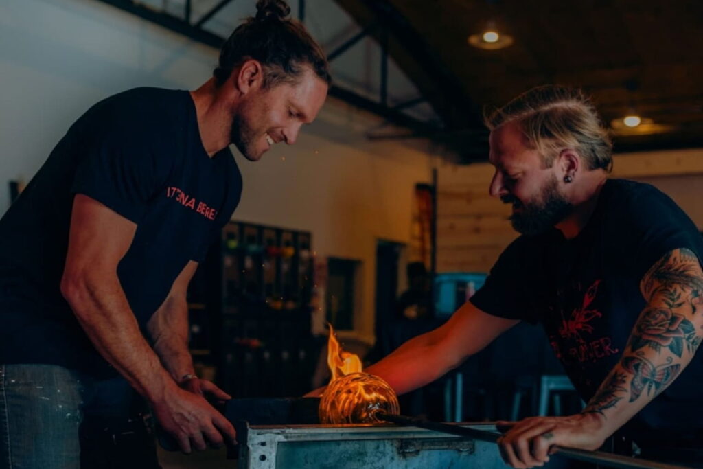 Two men over a flame at a glass blowing studio