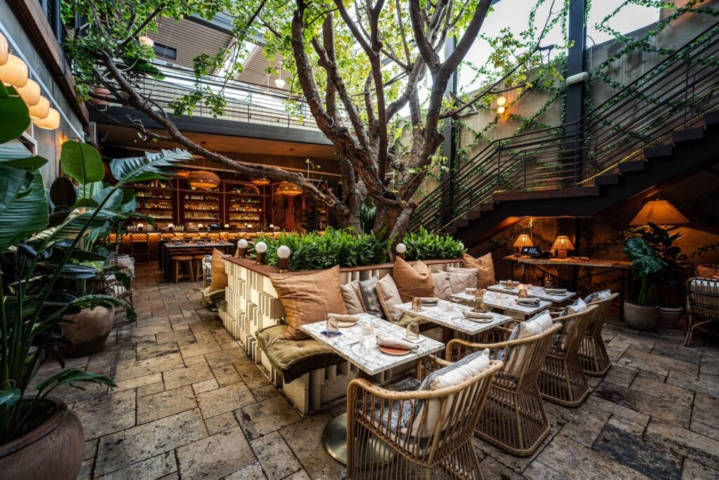 A Tulum-inspired restaurant space with wooden seating, soft lamplight and lush greenery