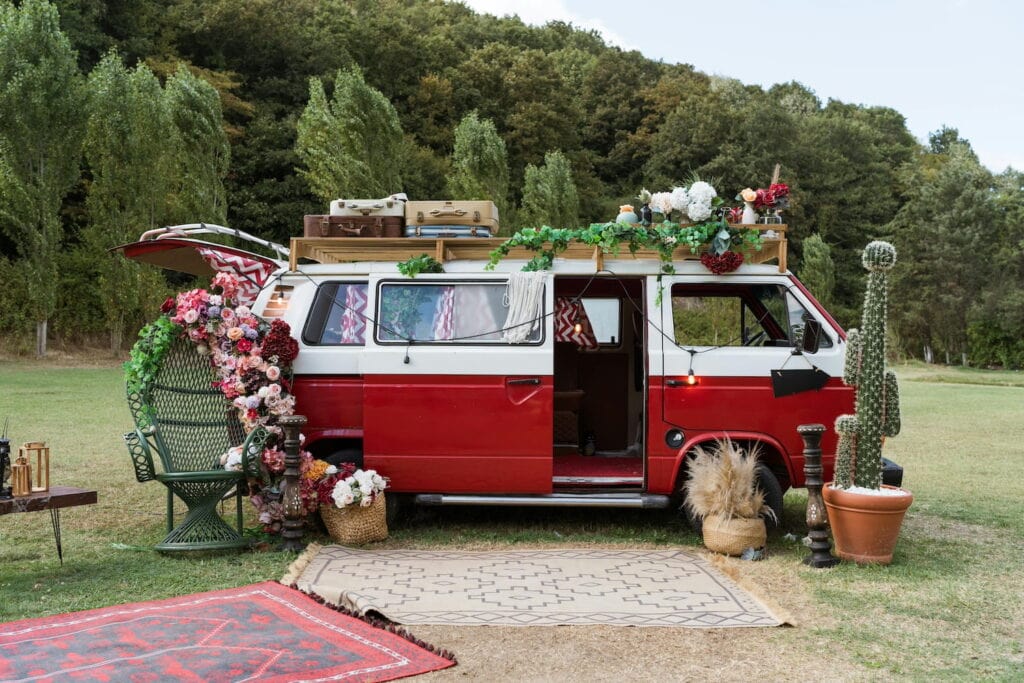 A red and white retro van sits in a field decorated with greenery and flowers