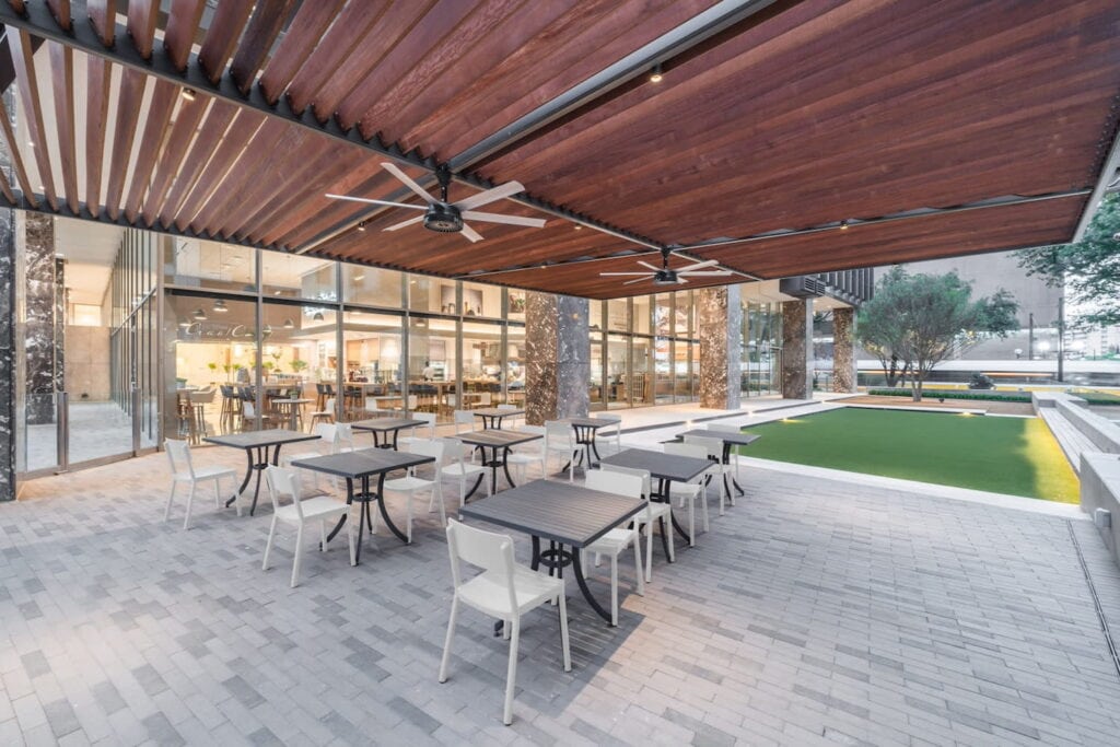 Covered patio area with small bistro tables outside cafeteria-like room of an office building