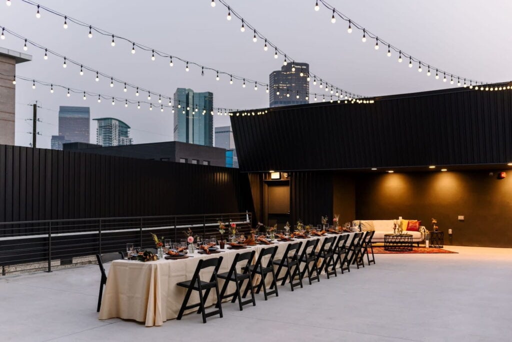 Rooftop dinner reception set up under string lights on vast outdoor patio with city views in background