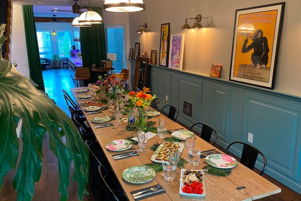 A long dining table in a rowhome dining room decorated with flowers and palm leaves