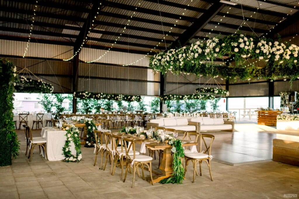 A rustic outdoor venue is set up with greenery and white florals, both on the tables and suspended from the high ceilings