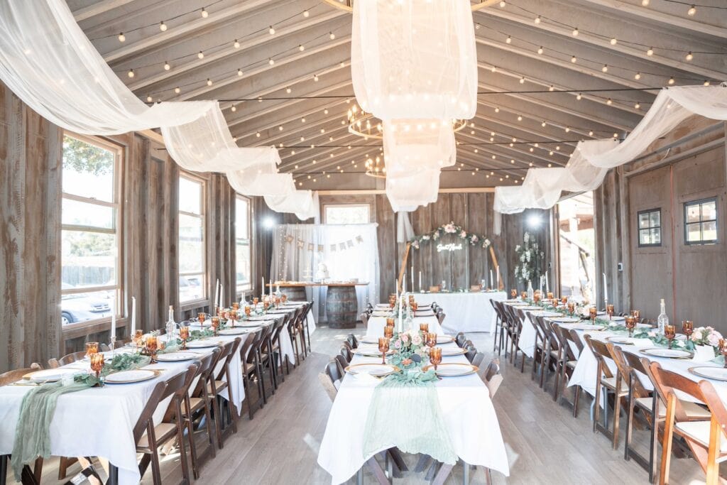 Long banquet tables are dressed in green and white at a wedding reception in a rustic barn setting