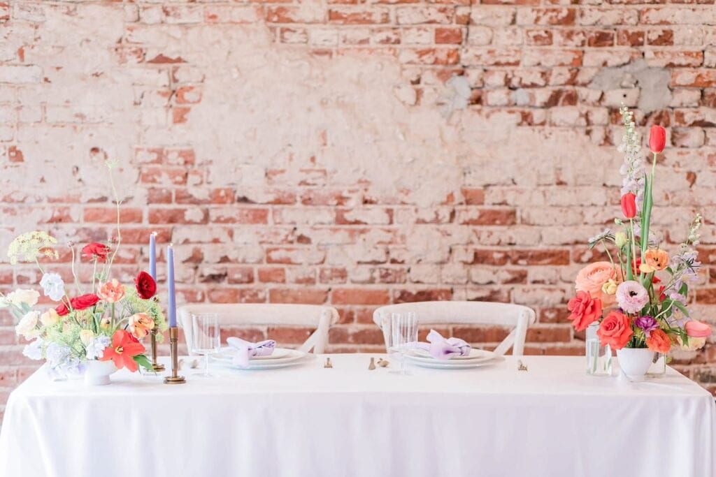 Simple head table at wedding reception by brick wall with romantic, whimsical floral arrangements