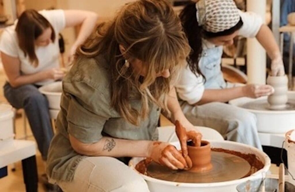 A woman forms clay on a wheel in a pottery studio