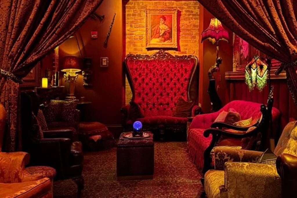 A sitting room decorated in red and gold velvet with dim lights and dark walls