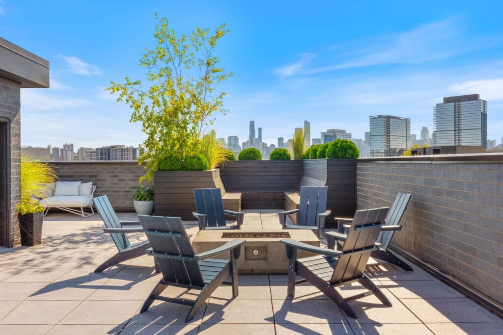 Adirondack chairs surround a fire pit on a Chicago rooftop with the city in the distance