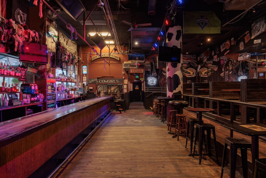 A saloon-inspired bar space in Seattle with dim lighting, wooden tables and cow print columns