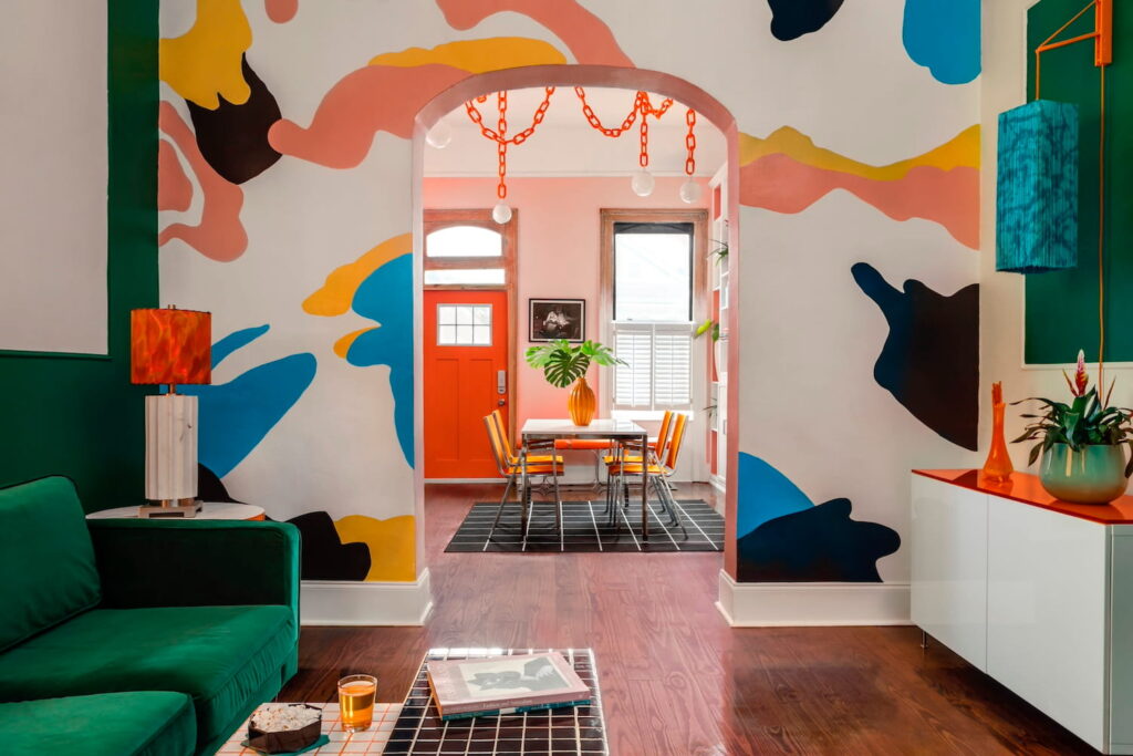 Brightly-colored interior of a house in New Orleans with abstract shapes painted on walls in primary colors, a bright orange front door, and dark green and orange accents