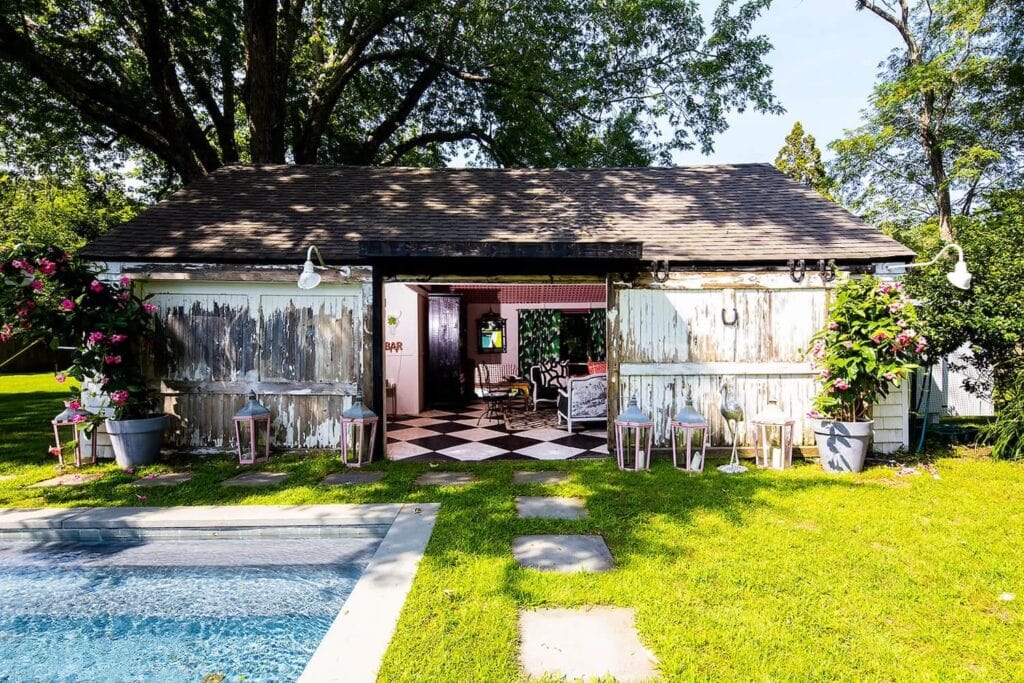 Shabby chic wooded shed with pink interior sits beside a glistening pool in the sunshine