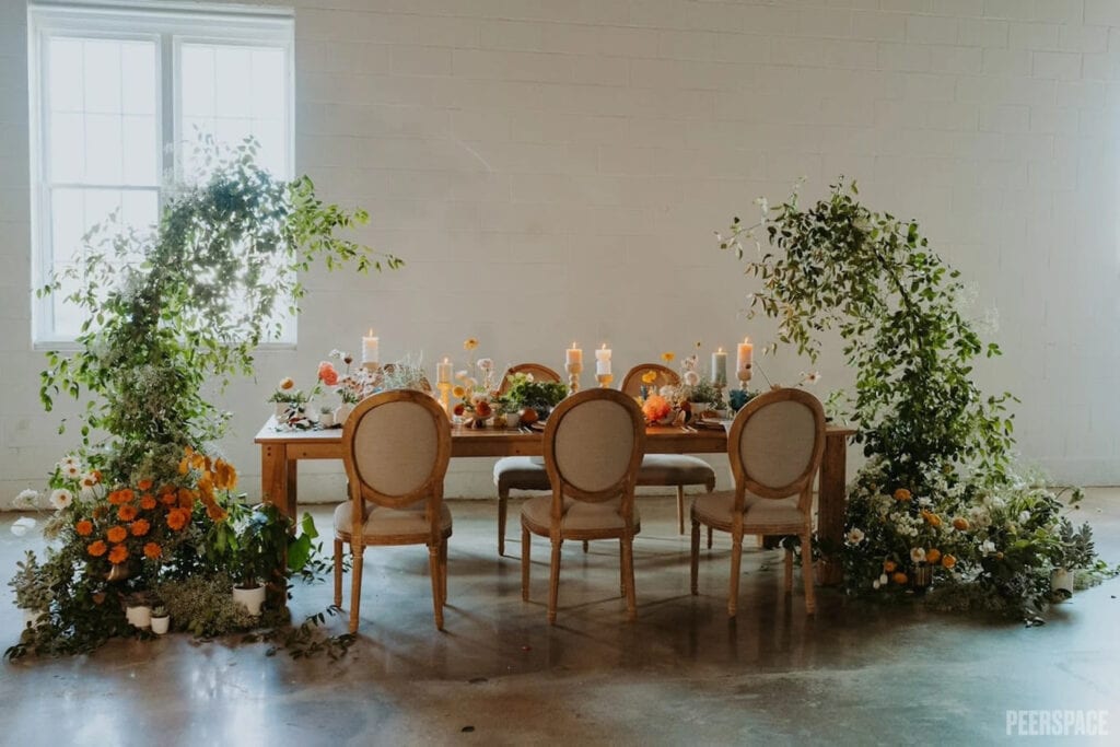 A small reception table is set with candles and flowers and flanked with large, arched floral arrangements
