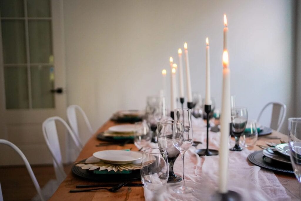 Close up photo of a simply set dining table with tall candles in black candlesticks, clear glassware and white plates