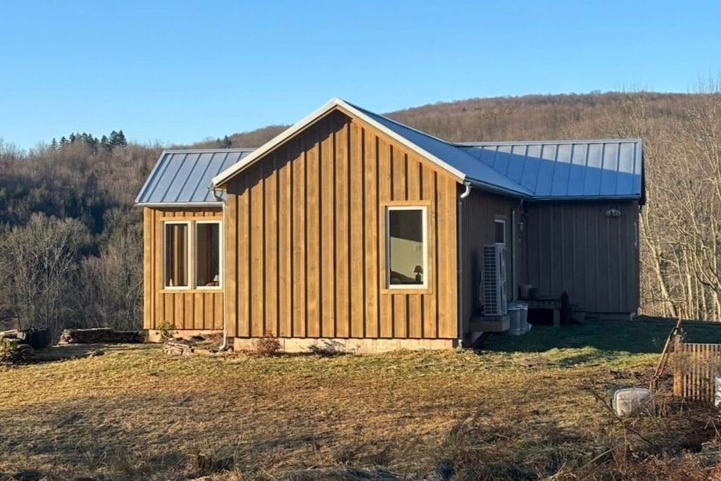 A small wooden structure sits on a farm with a hilly backdrop in the distance