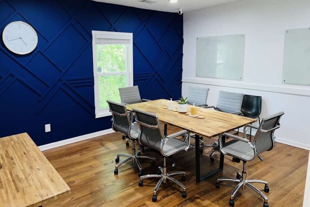 A small conference room with wooden tables, gray chairs and a dark blue accent wall
