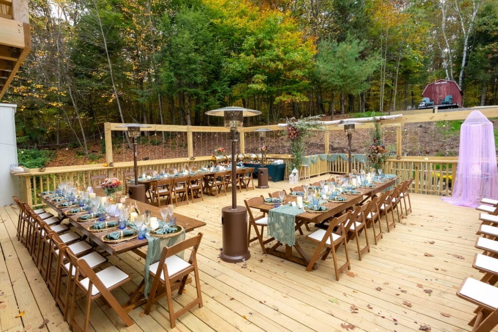 Simply decorated, long dining tables are set up under heat lamps on a deck with a red barn in the distance