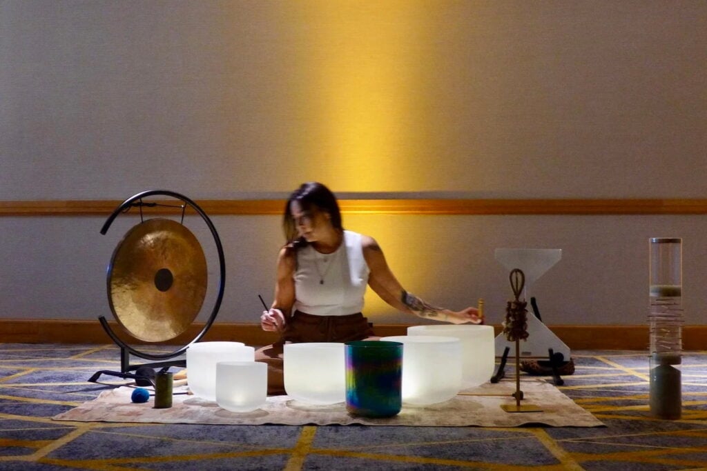 A woman sits on the floor in dim lighting performing a sound bath
