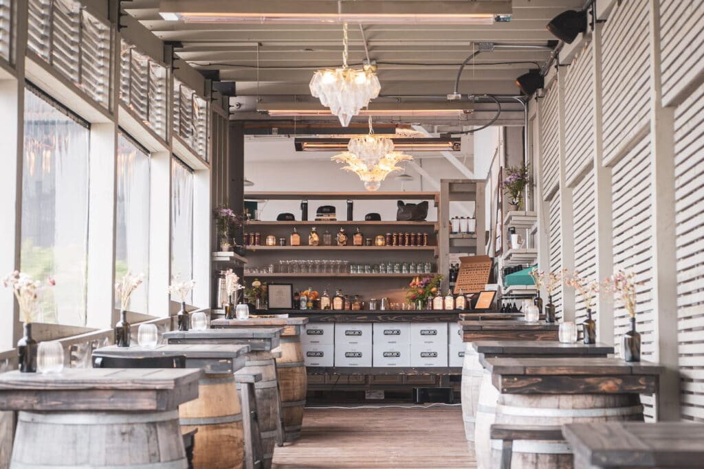 Rustic speakeasy space in Seattle with wooden tables crafted from wine barrels, a large bank of windows and a tall bar in the back