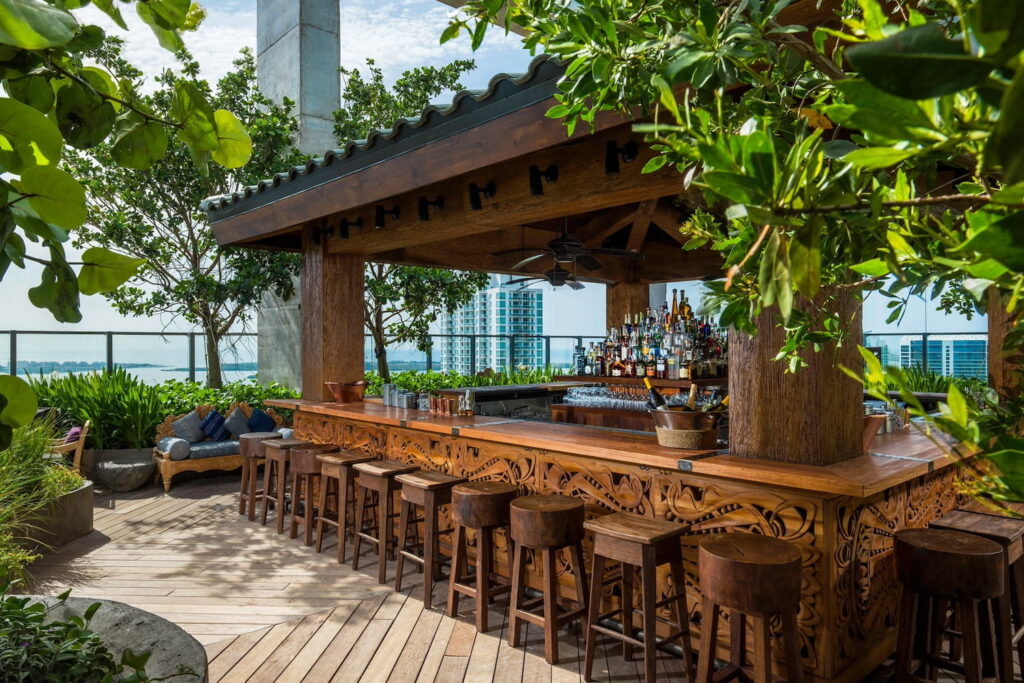 Ornately carved wooden bar with matching wooden stools on a rooftop in Miami