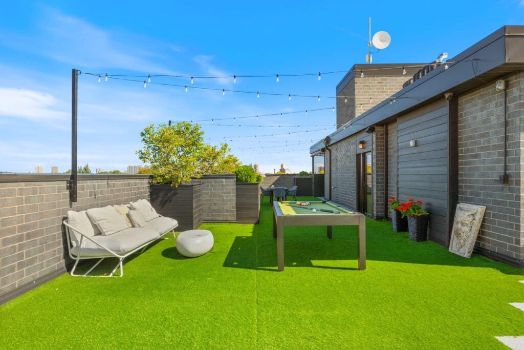 A pool table sits under string lights and next to outdoor couches on a rooftop gathering space