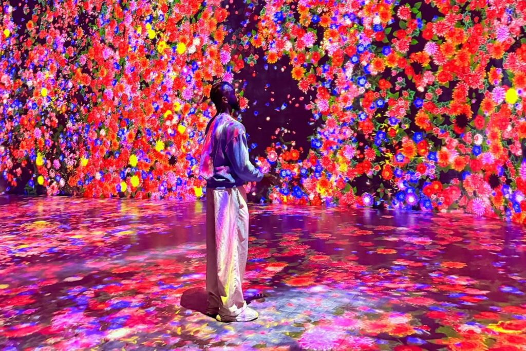 A man stands in an open room illuminated with neon floral imagery on the floor and walls