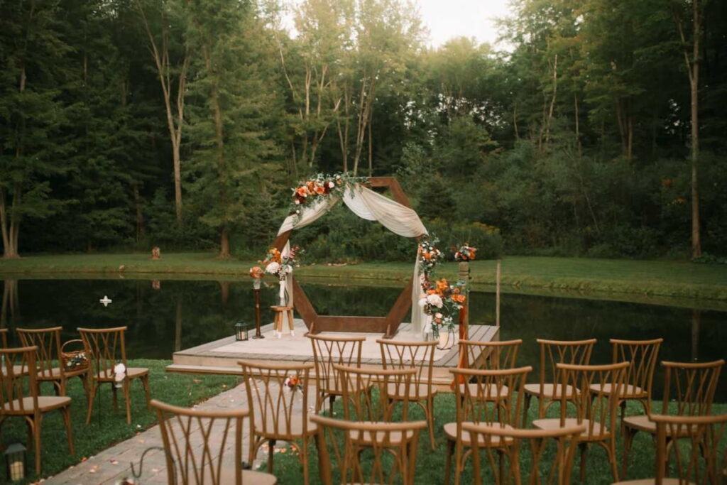 Wedding ceremony set up outside next to a lake with a wooden altar on a dock draped in gauze and decorated with flowers