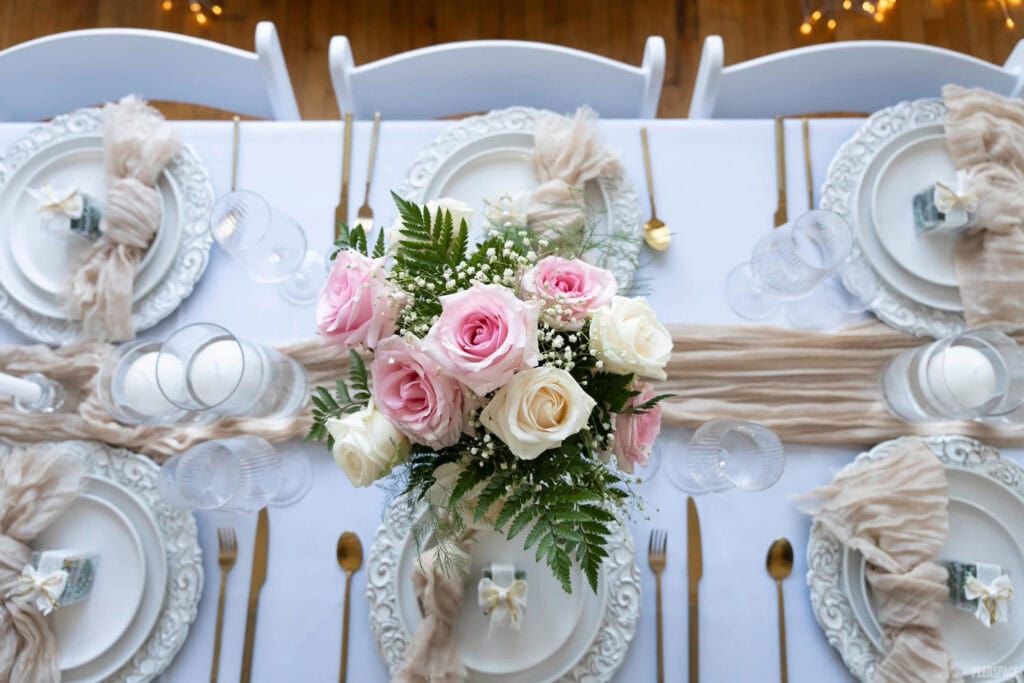 Pink and white roses are the centerpiece of a guest table set with white place settings and gold cutlery