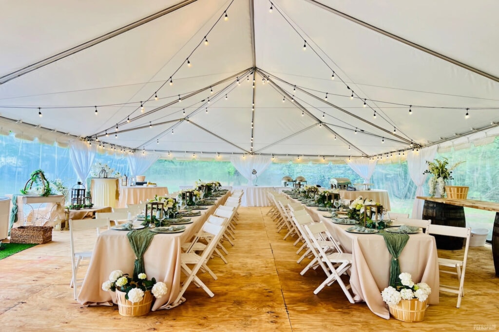 Long guest tables decorated in cream and green sit under a giant reception tent lit up by string lights