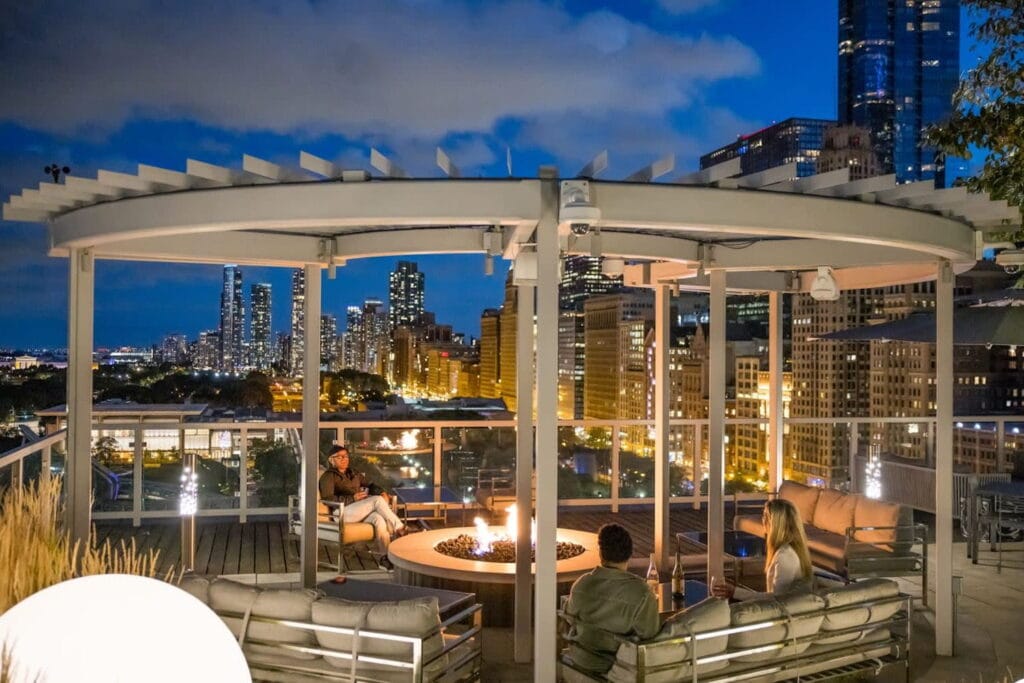 Friends gather around a fire pit on a Chicago rooftop with views of the skyline