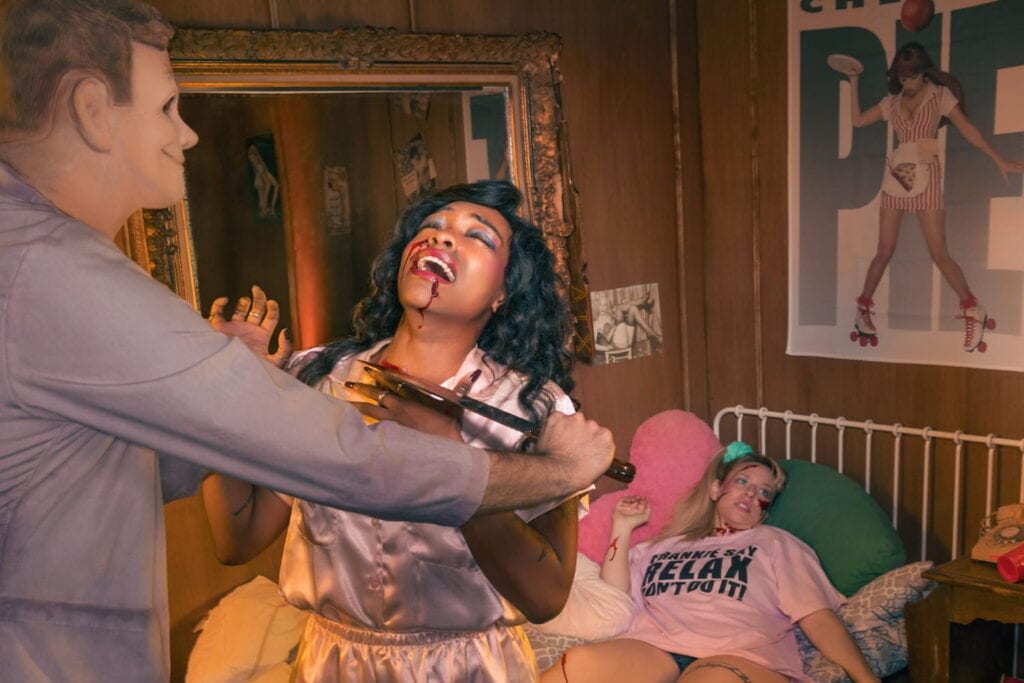 A still shot from a scene out of an immersive horror takeover of a man in a mask appearing to slash two women with a knife