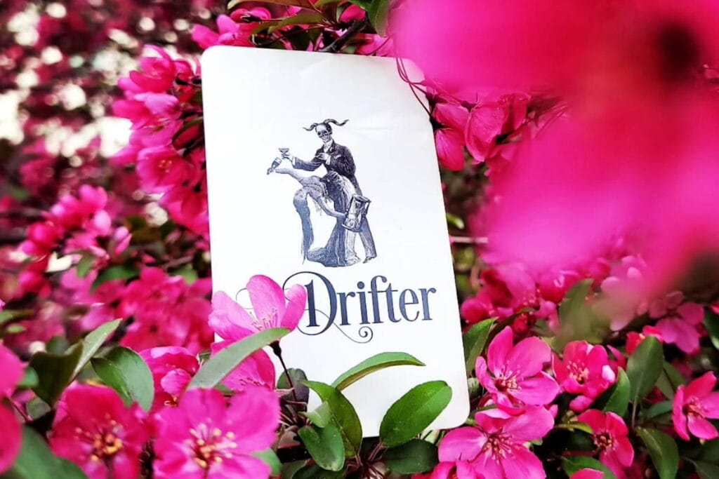 A card with The Drifter logo on it sits in a batch of pink flowers