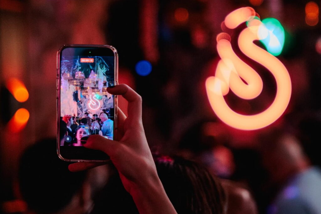 Close up of a hand holding a cellphone in camera mode taking a photo of a party scene