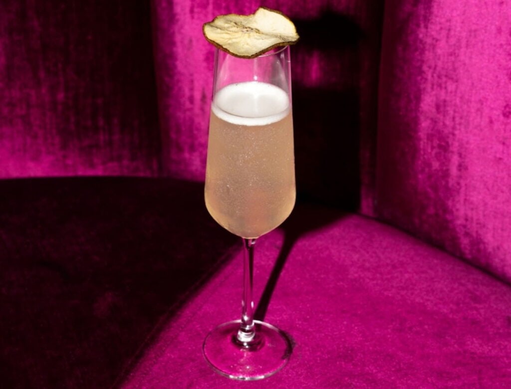 A glass of champagne sits on a pink velvet chair