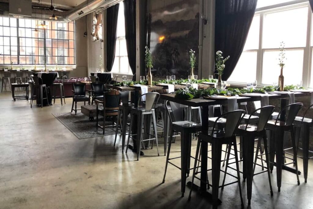 Modern, industrial winery dining area with a mix of high top and low top tables, large windows and dramatic draperies