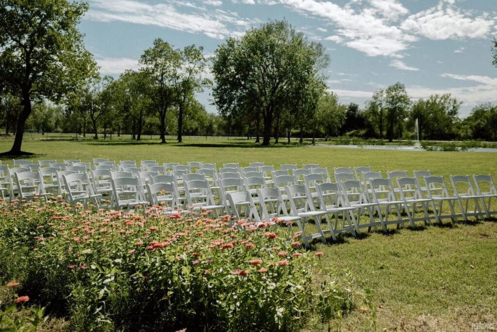 White chairs are set up outside in a vast meadow for a wedding reception
