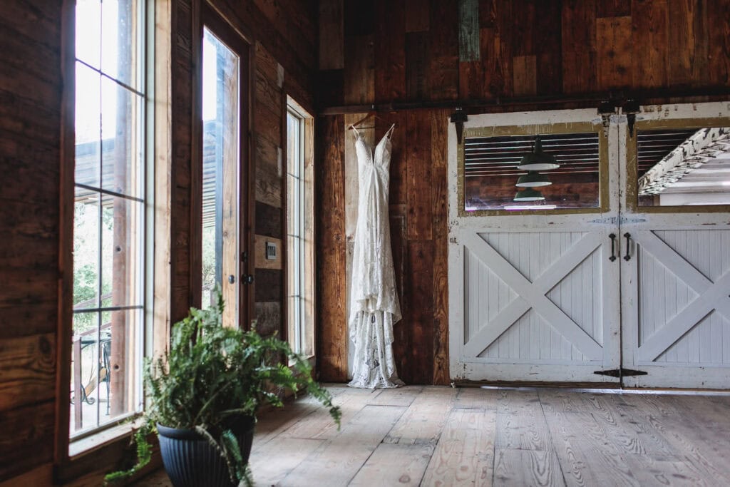 A wedding dress hangs against a wooden wall next to large barn doors