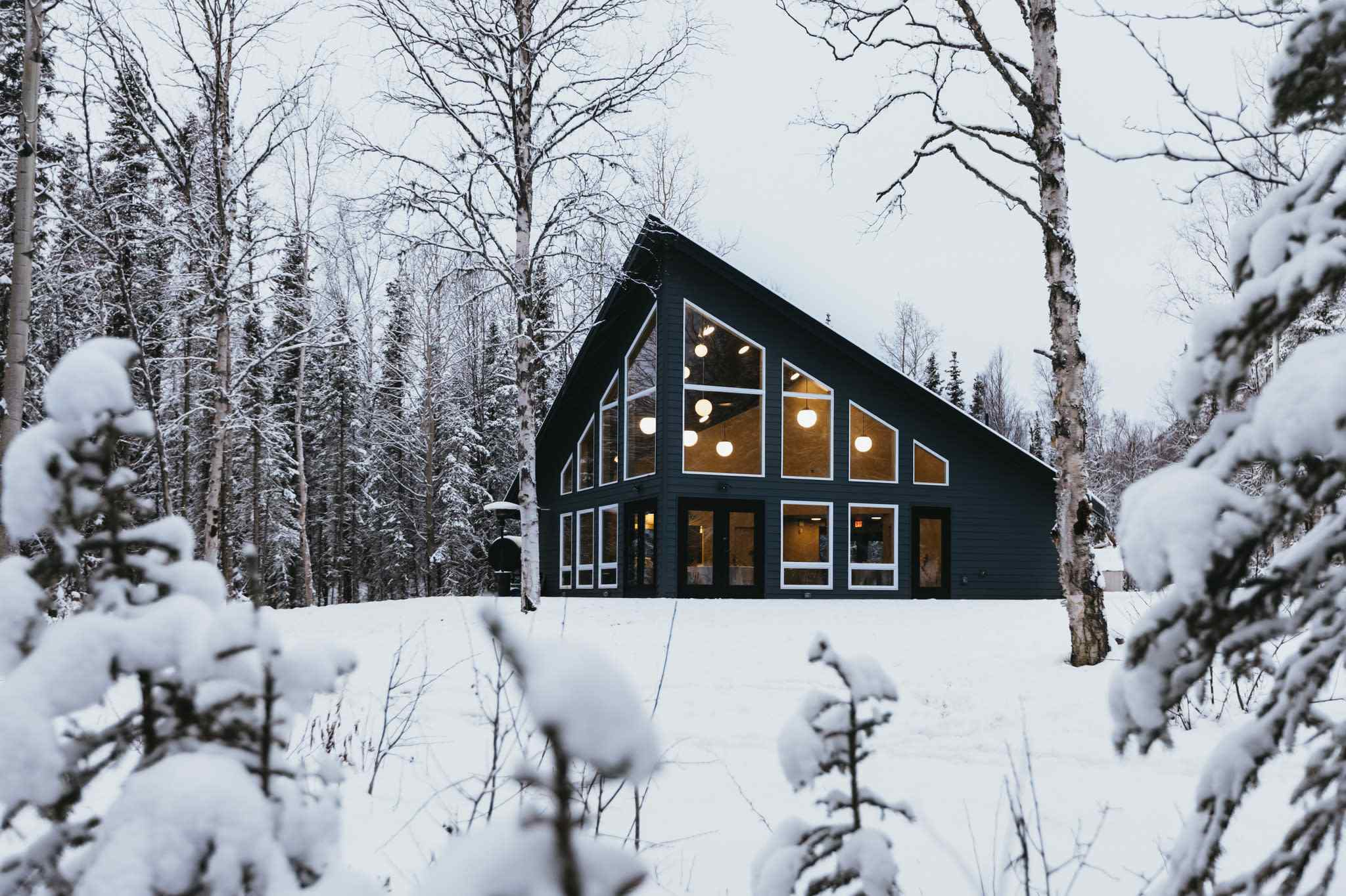 Modern black cabin with glowing windows in snowy Anchorage wilderness