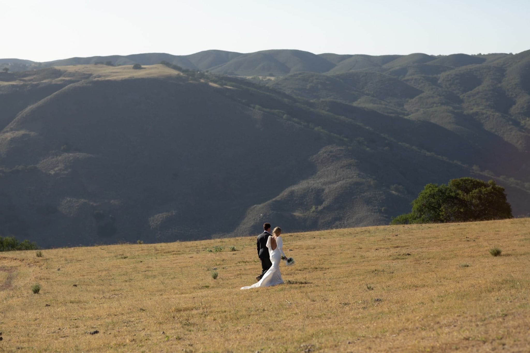 Bride and groom walking through scenic Fresno hillside landscape