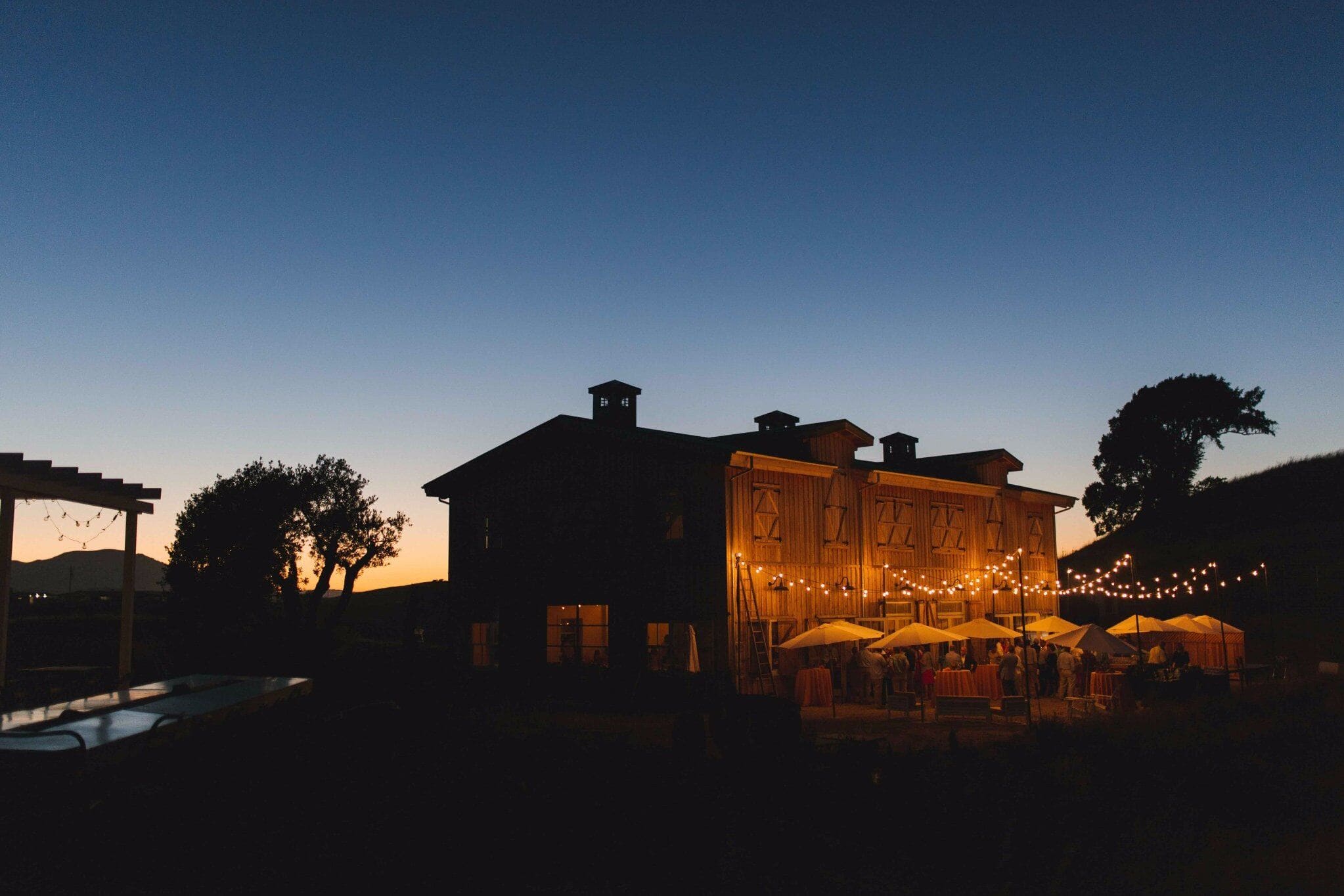 Rustic Fresno barn wedding venue illuminated at twilight with string lights