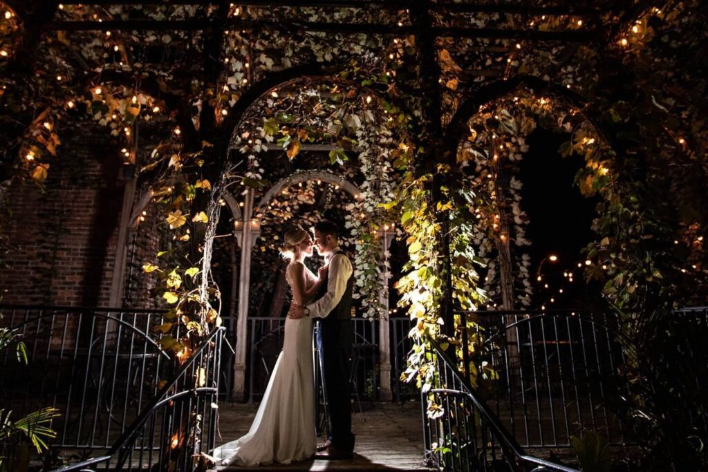Bride and groom standing under leaf-wrapped archway with fairy lights at nighttime wedding in Georgia