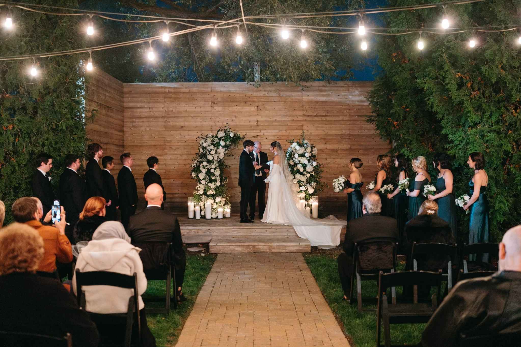 Outdoor nighttime Missouri wedding ceremony with string lights and florals