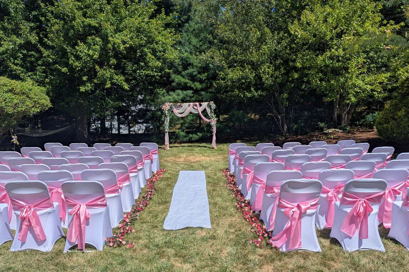 Waterside garden wedding ceremony with pink chairs and arbor in Rhode Island